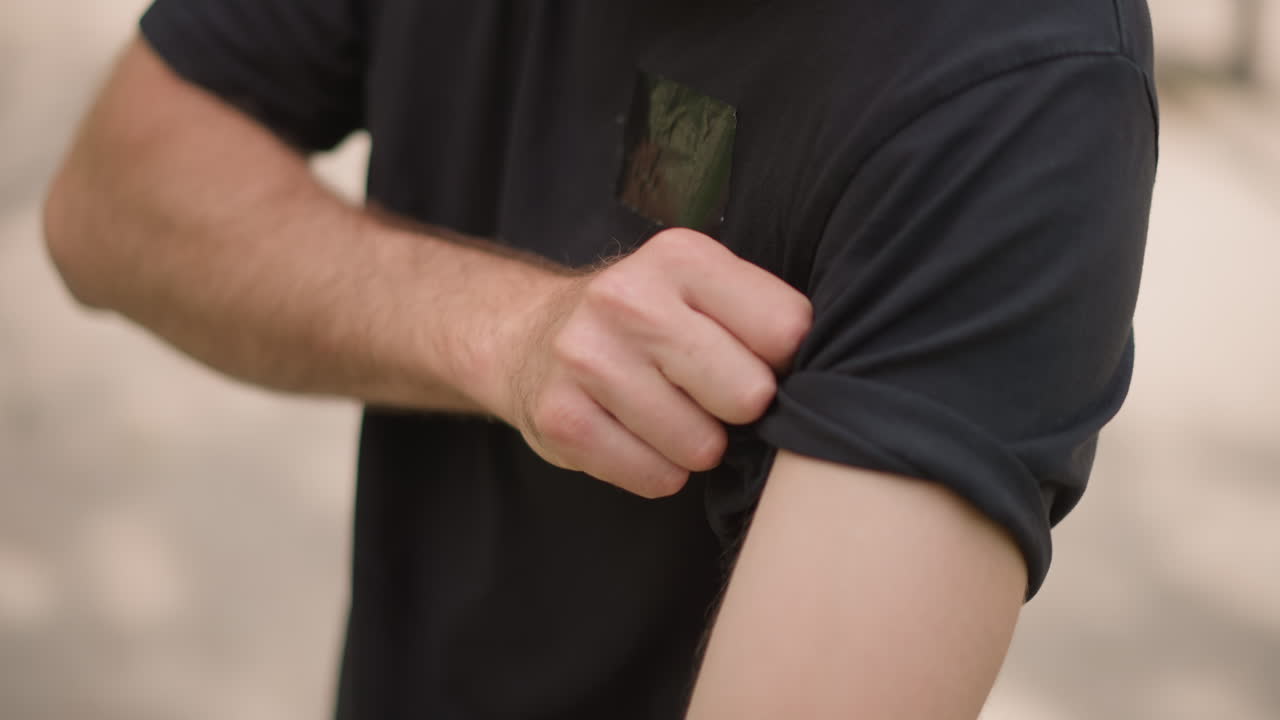 Man Adjusts Sleeve Thoughtfully In Bright Sunlight, Man Gently Rolling His Shirt Sleeve Outdoors Under Warm Light, Closeup Of Man Deliberately Rolling His Shirt Sleeve In Outdoor Sunlight