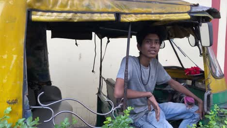 a young indian auto driver in grey t-shirt sitting inside the auto looking at the camera