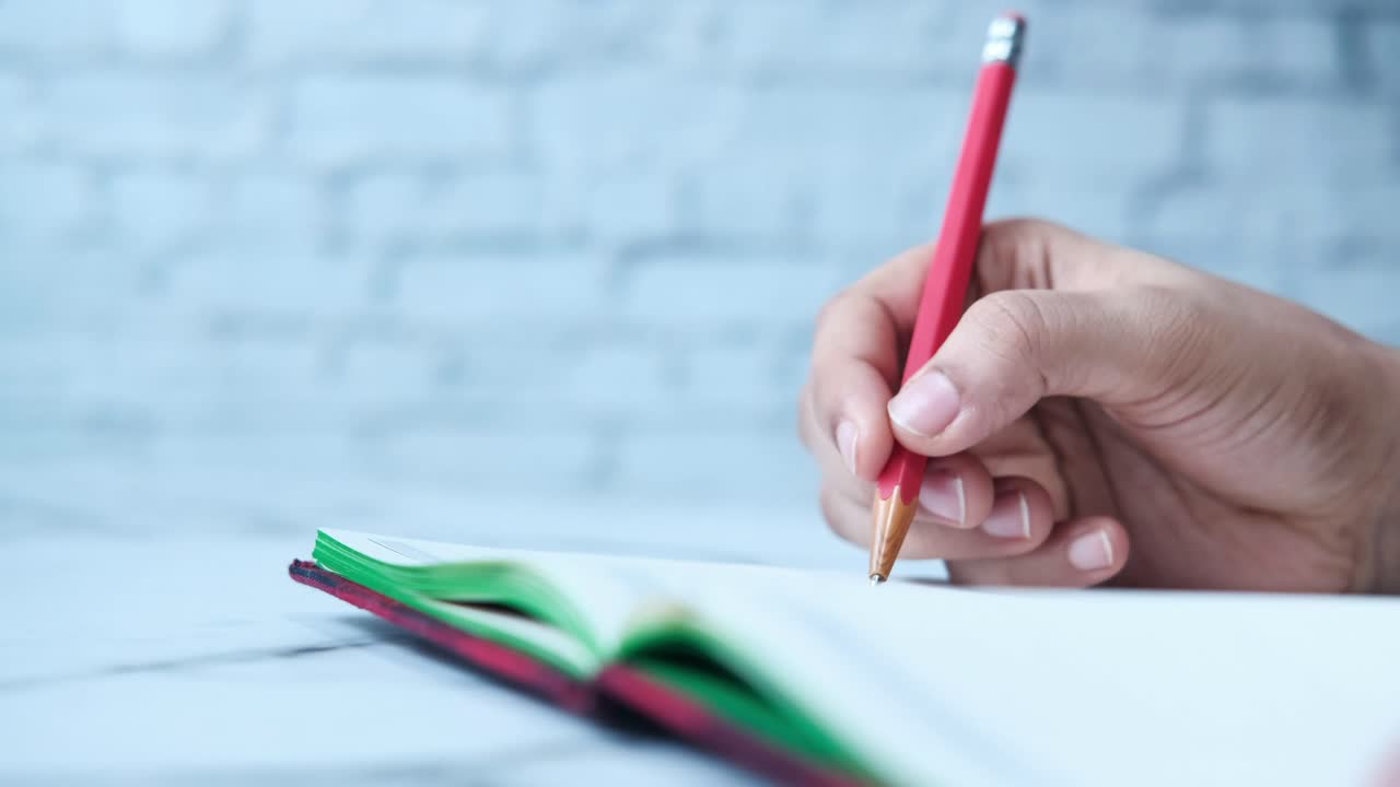 persona escribiendo en un cuaderno con un lápiz rojo