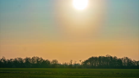 Orange-glow-sun-goes-up-blue-skyline-above-green-agricultural-fields-time-lapse