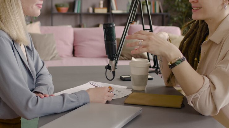 Primo piano di due donne che registrano un podcast parlando in un microfono sedute alla scrivania
