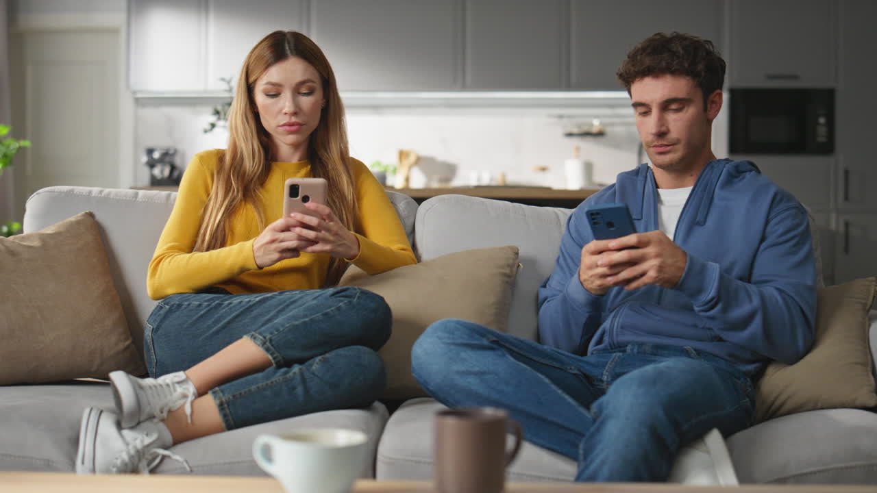 Offended pair browsing smartphones at home weekend. Worried man looking at woman