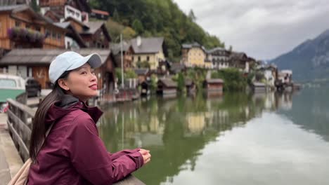 camera shifts focus from asian woman to the lakeside village of hallstatt, austria, on a rainy autumn day with alpine scenery