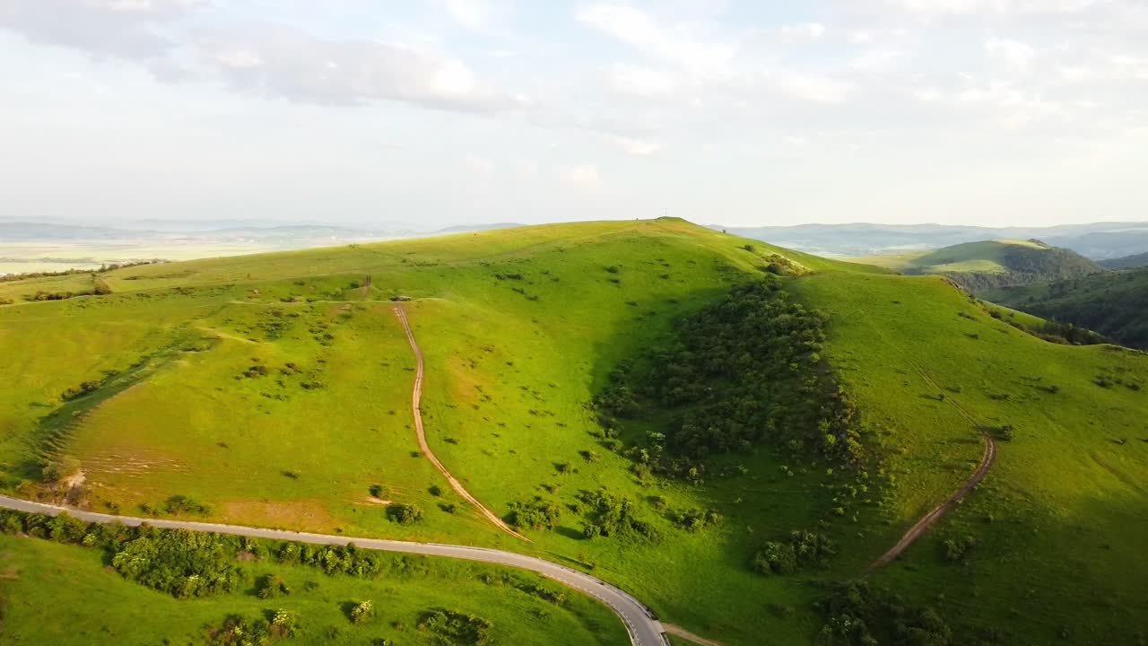 Aerial sunrise view of peaceful Romanian lush green fields and Carpathian mountains, beautiful rural landscape under soft golden morning light.