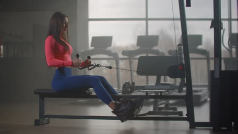 La-Mujer-Con-Un-Cuerpo-Fuerte-Y-Delgado-Con-Leggins-Azules-Y-Top-Rosa-Realiza-Un-Ejercicio-En-Los-Músculos-De-La-Espalda-Y-Los-Omóplatos-En-El-Gimnasio.-Entrenamiento-Productivo-Para-Un-Cuerpo-Sano.