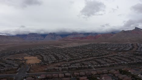 Wide-aerial-panning-shot-of-Red-Rock-Canyon-behind-desert-suburb-community-in-Las-Vegas,-Nevada