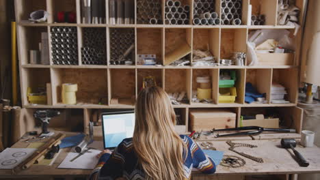 Rear-View-Of-Female-Designer-In-Workshop-Working-Late-On-Components-For-Hand-Built-Bicycle