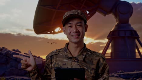 close up of asian man soldier using a tablet and pointing to side while standing with satellite dish