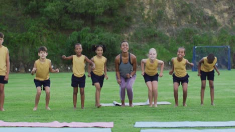 Mixed-race-female-teacher-and-diverse-group-of-schoolchildren-jumping-and-smiling-outdoors