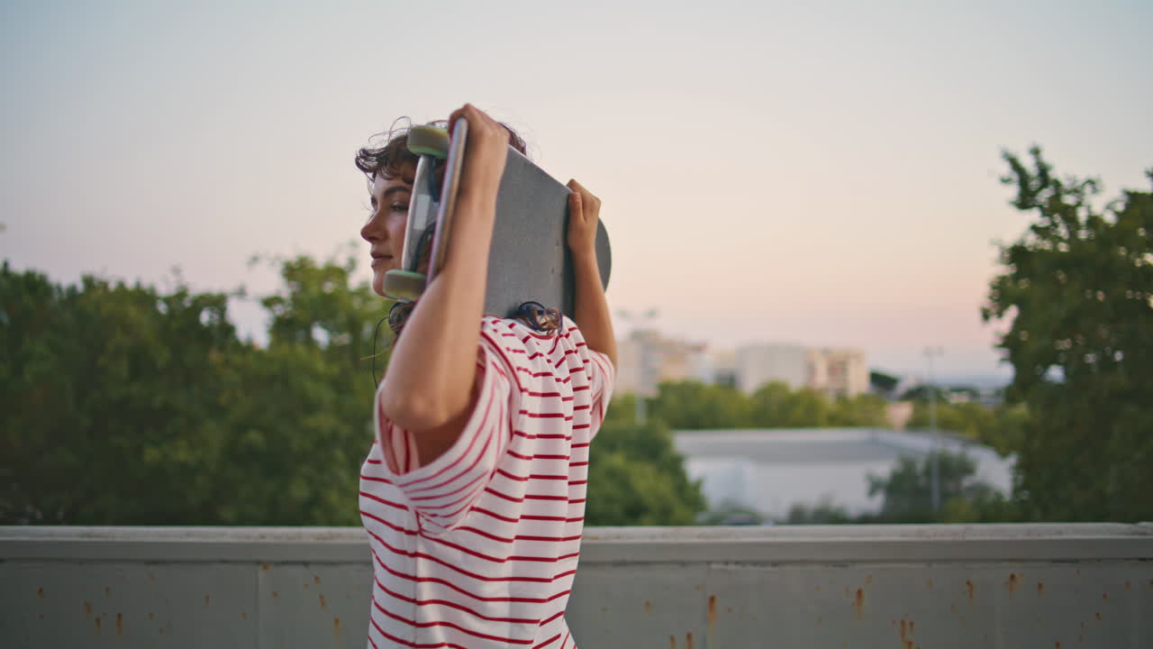 joven patinador mirando la cámara sosteniendo longboard en los hombros de cerca.