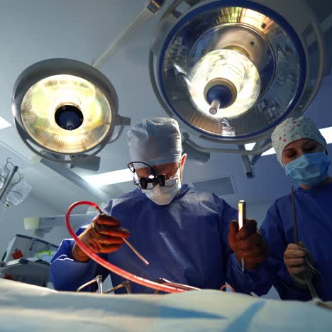 medical team perform an operation under surgical lamp. front view of a surgeon and female assistant doing a surgery using special medical tools