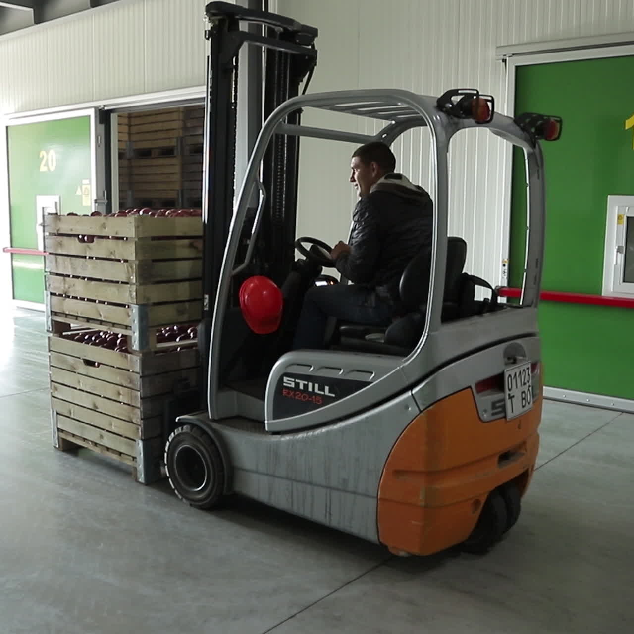 A worker moves two wooden crates of ripe apples using a forklift to the designated storage room in the warehouse of the plant. Working process.