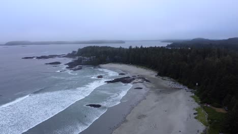 Küste-Von-Tofino-Mit-Nebligem-Himmel,-Wellen,-Die-Am-Sandstrand-Brechen,-Umgeben-Von-üppigem-Wald