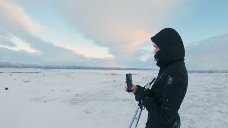 female cross country skier filming and takes photos of her friend with her mobile phone on a mountain in the northern sweden