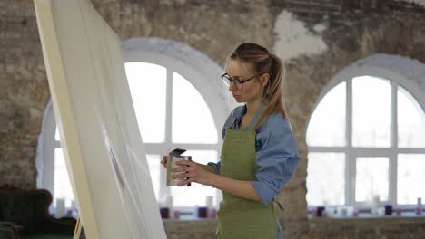 female artist working with large paintbrush standing in front wide canvas