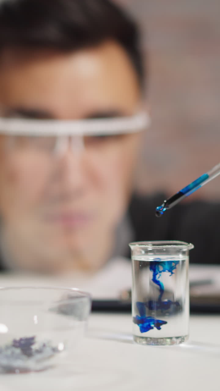 Student guy with white gloves drops dark blue liquid into beaker with clear water doing research in medical college laboratory close view