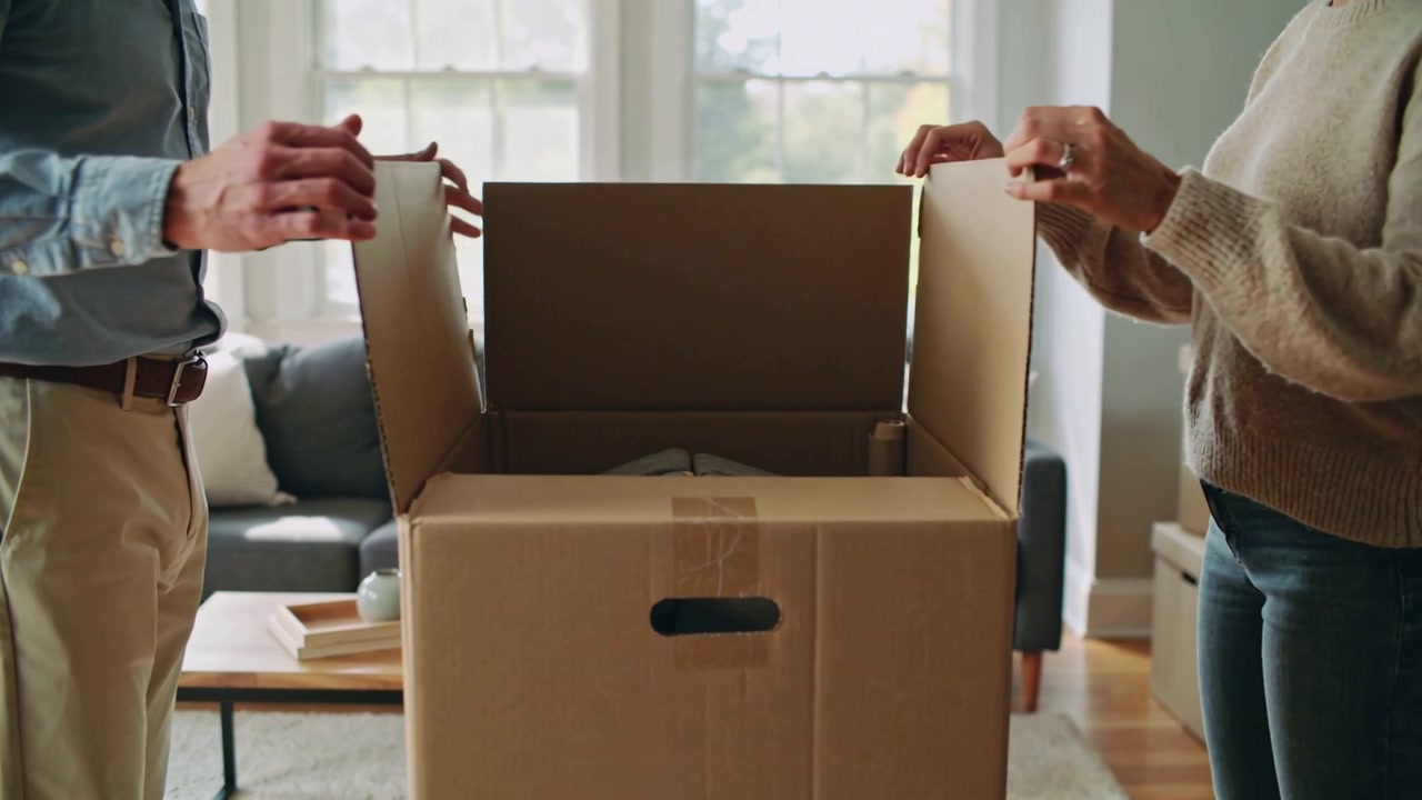 Placing hands, man blue shirt and woman knit sweater lifting box flaps at home, inspecting item