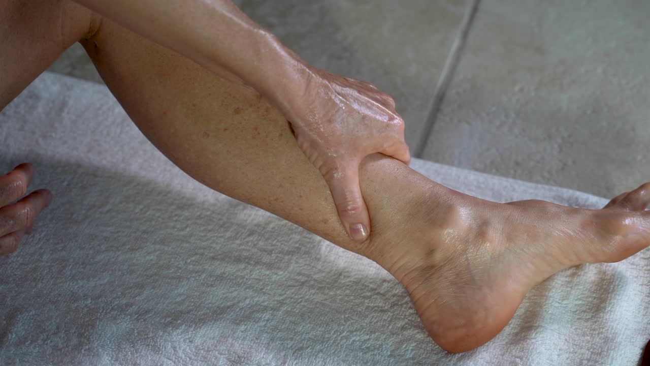 Side view of woman with oil on her hands rubbing and twisting her calf preparing for gua sha and myofascial massage