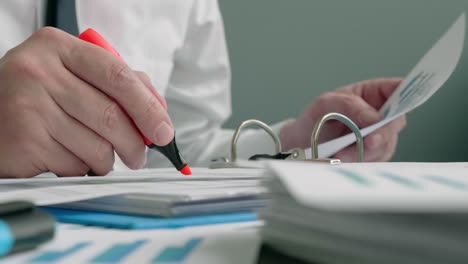 a hand with a marker with which the auditor makes notes on a stack of papers.