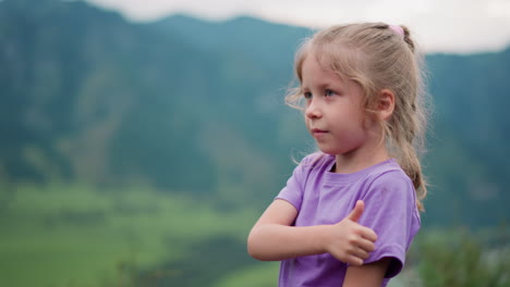 Positive-little-child-shows-thumb-up-gesture-in-green-valley