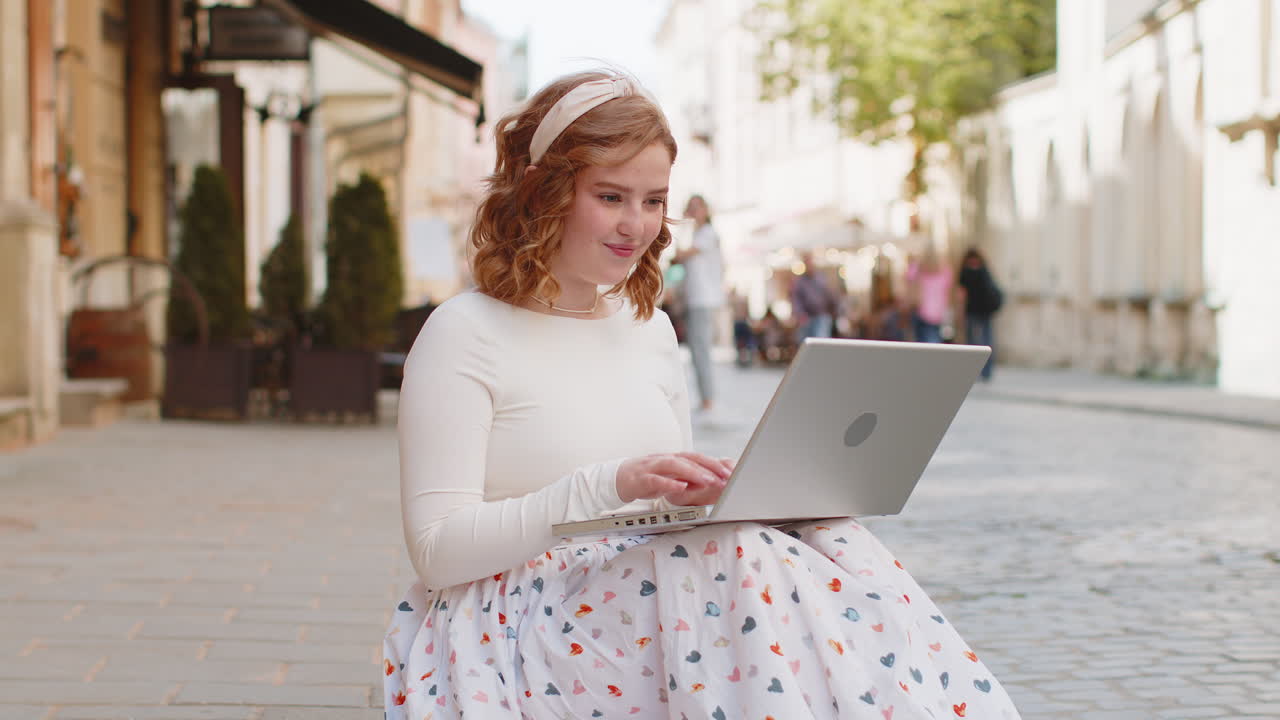 Caucasian woman freelancer sits on city street using laptop working online distant job during break
