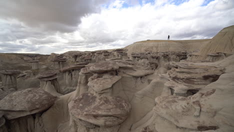 figura humana solitaria caminando en la cima del acantilado sobre formaciones de arenisca de hongos en el desierto de bisti de-na-zin, nuevo méxico, ee.uu.