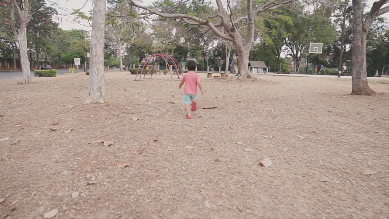 Energetic  two year old Asian boy enjoying playing and running free among trees at a park with an outdoor playground
