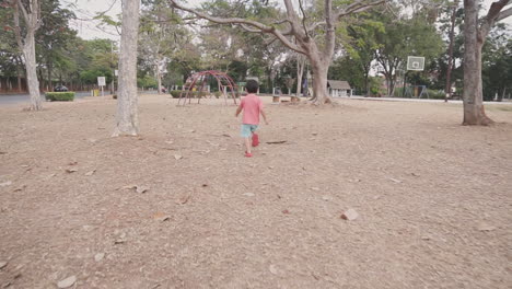 energetic  two year old asian boy enjoying playing and running free among trees at a park with an outdoor playground