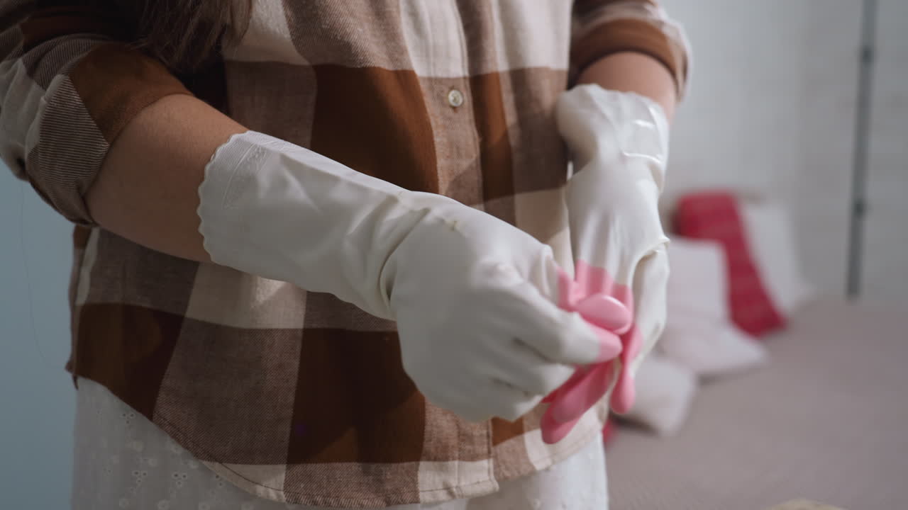 Harvester removes one white rubber glove with pink fingertips after tending indoor plants by glass door and brick wall, revealing clean hand and showcasing gardening routine in cozy home greenhouse