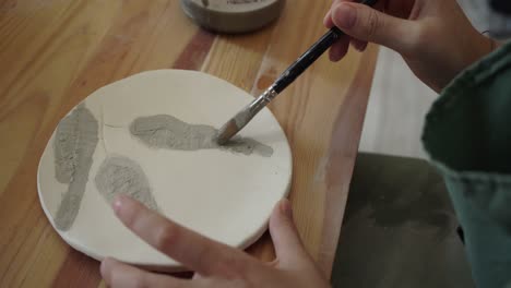 close up of artist painting detail onto a ceramic dish