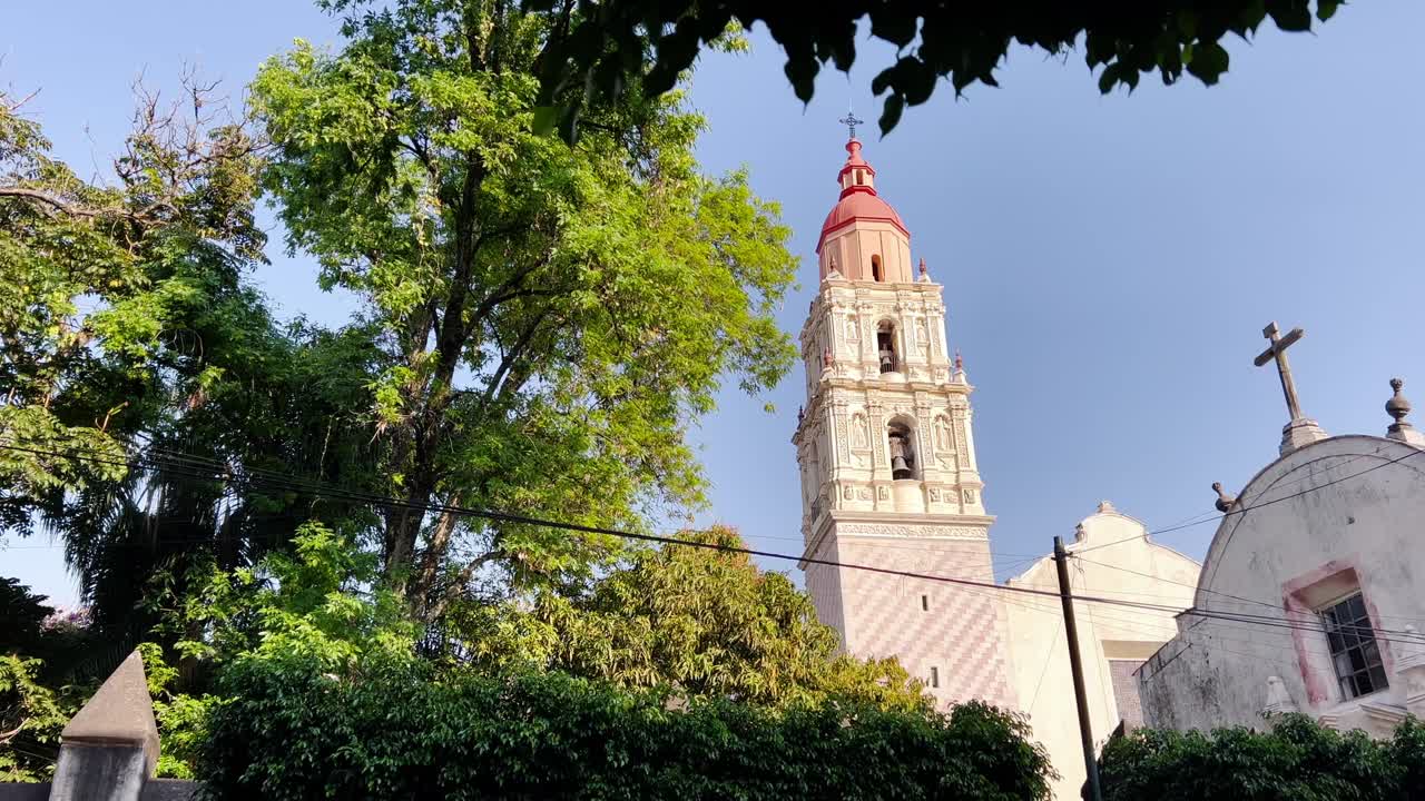 Framed view of Cuernavaca's Cathedral bell tower with green trees and blue sky in Cuernavaca, Mexico