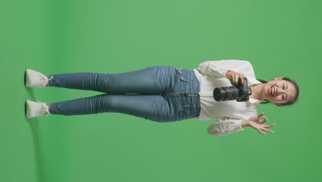 full body of asian photographer using a camera taking picture and showing okay gesture while standing on green screen background in the studio