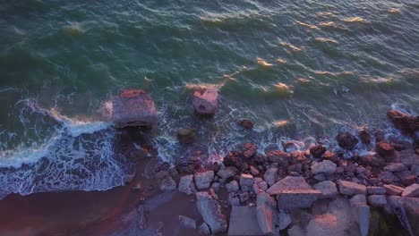 Aerial-birdseye-view-of-abandoned-seaside-fortification-buildings-at-Karosta-Northern-Forts-on-the-beach-of-Baltic-sea-,-waves-splash,-golden-hour-sunset,-drone-dolly-shot-moving-left