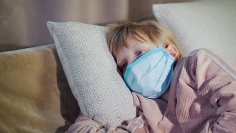 sick child lies in bed in a gauze mask