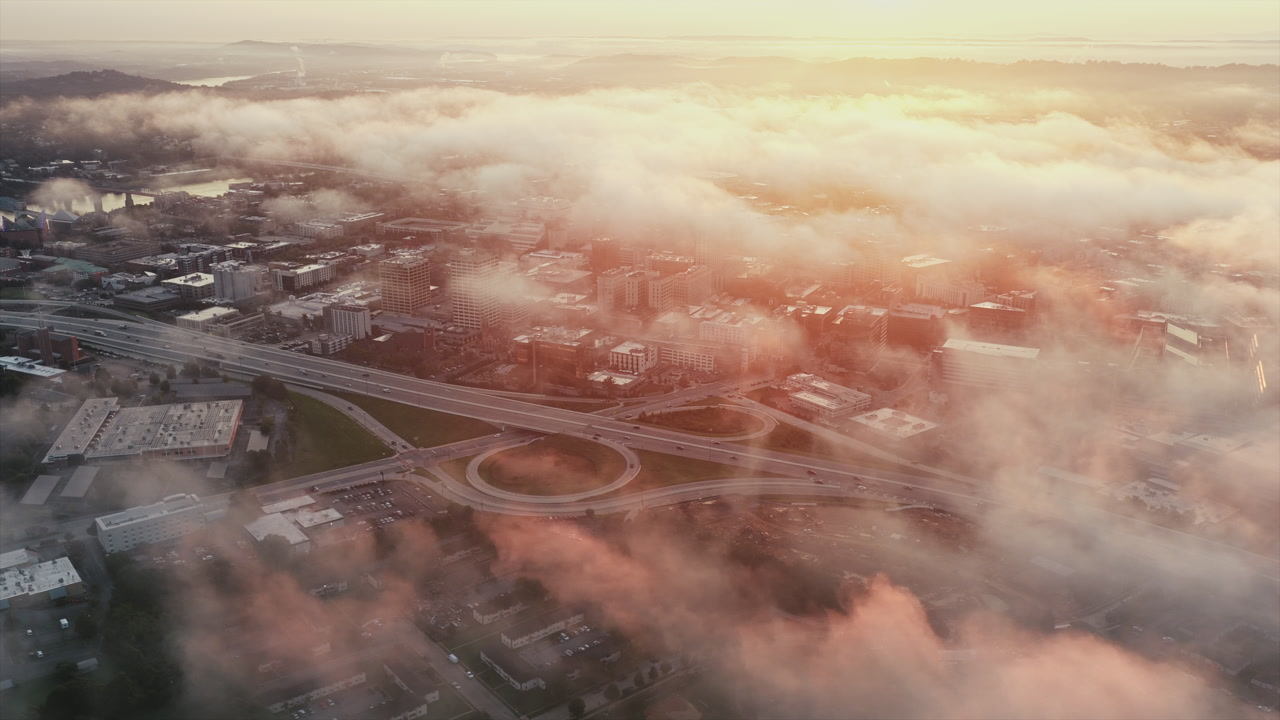 Fog drifts over Chattanooga’s downtown as sunrise paints highways and city streets in a golden glow.