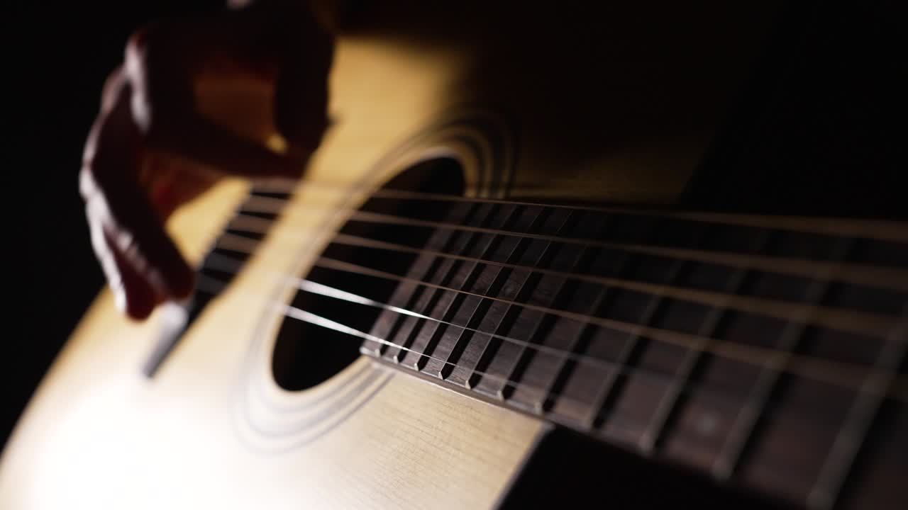 Musician plays acoustic guitar sitting in dark room