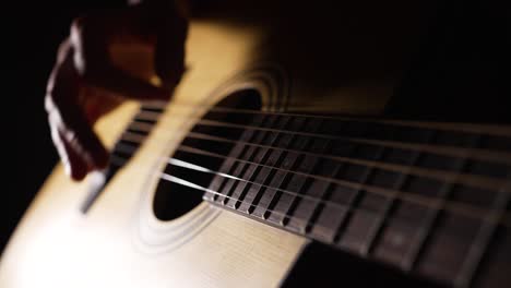 musician plays acoustic guitar sitting in dark room