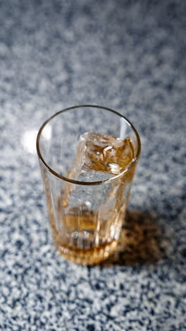 thick yellow liquid syrup is poured into the glass with ice cube. making a cocktail. close up. top view. vertical video.