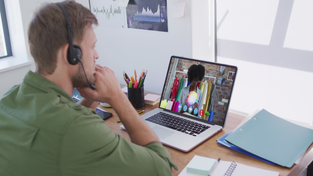 En kaukasisk mand med telefonheadset holder et videomøde med en kvindelig kollega på sin bærbare computer på kontoret.