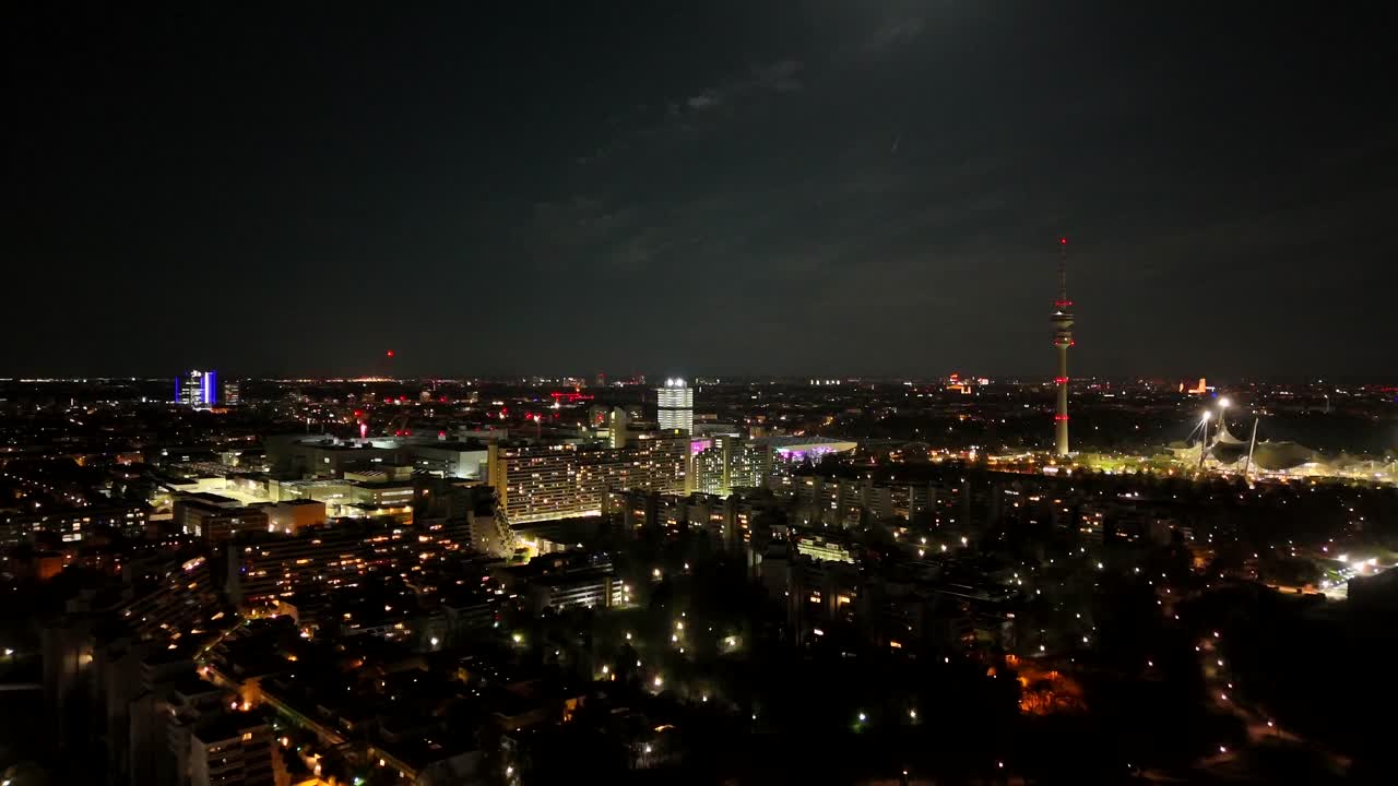 Lighting cityscape of Munich Town at night. Aerial forward wide shot. The Olympic Tower and illuminated city in district. Panorama view. Housing area and Suburb neighborhood.