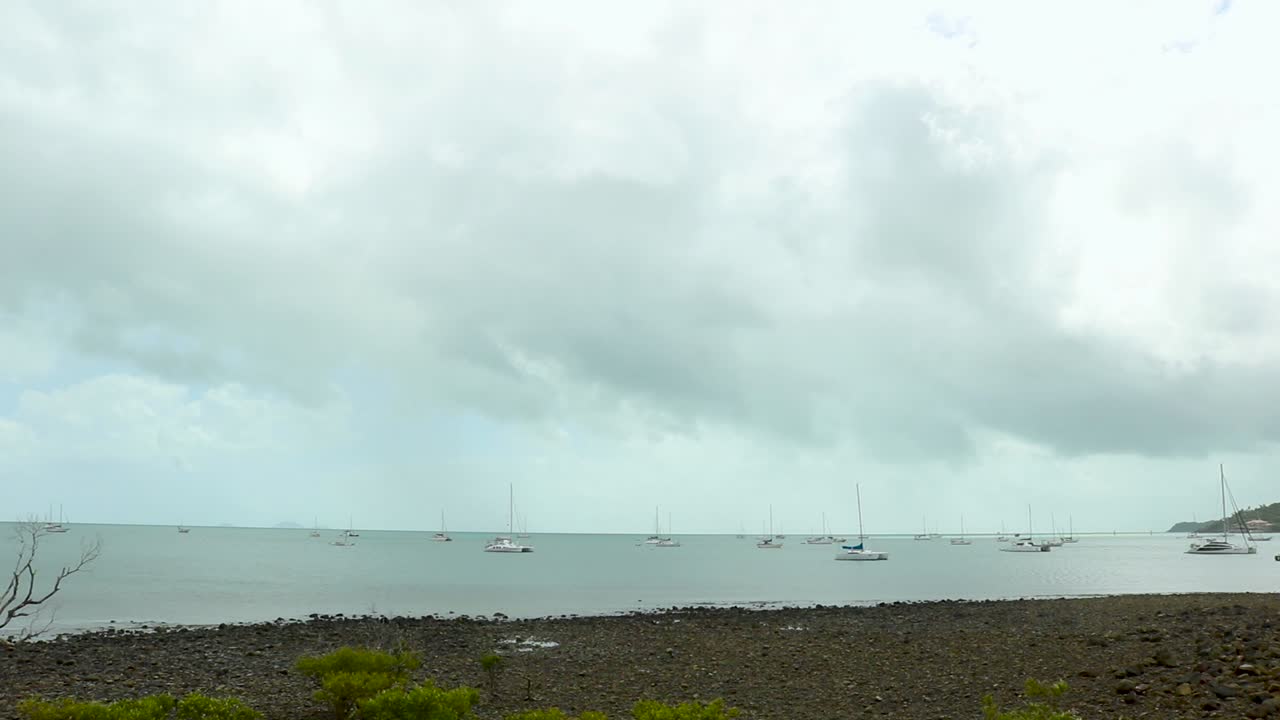 A dozen boats sit on the water under large grey clouds in Airlie Beach, Australia.