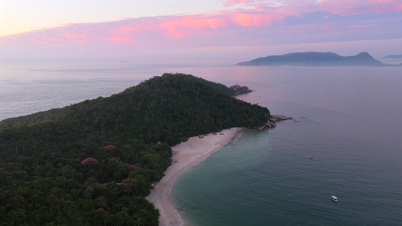 Secluded white sand beach and crystal clear turquoise shoreline at Ilha do Campeche under pink dawn sky. Slow motion aerial descent.