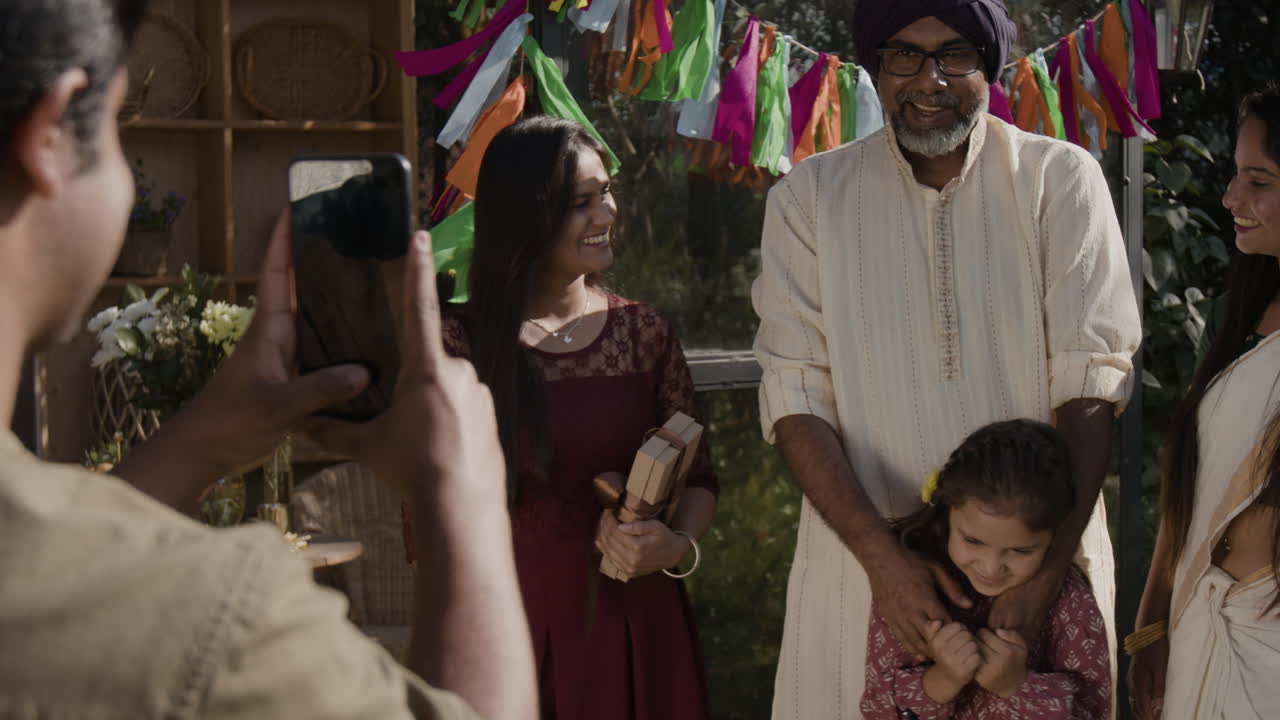 A family celebrates outdoors with gifts, capturing joyful moments on a smartphone