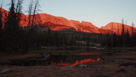 Impresionante-Toma-De-Paisaje-De-Lapso-De-Tiempo-Del-Hermoso-Lago-De-Mariposas-Rodeado-De-Grandes-Montañas-Rocosas-Y-Pinos-Dentro-Del-Bosque-Nacional-Uinta-Wasatch-Cache-En-Utah-Durante-Una-Puesta-De-Sol-De-Verano