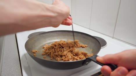 man stirring wheat protein slices in a frying pan with a spatula