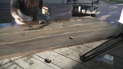 a man staining a table he is building with a large brush and with its second coat