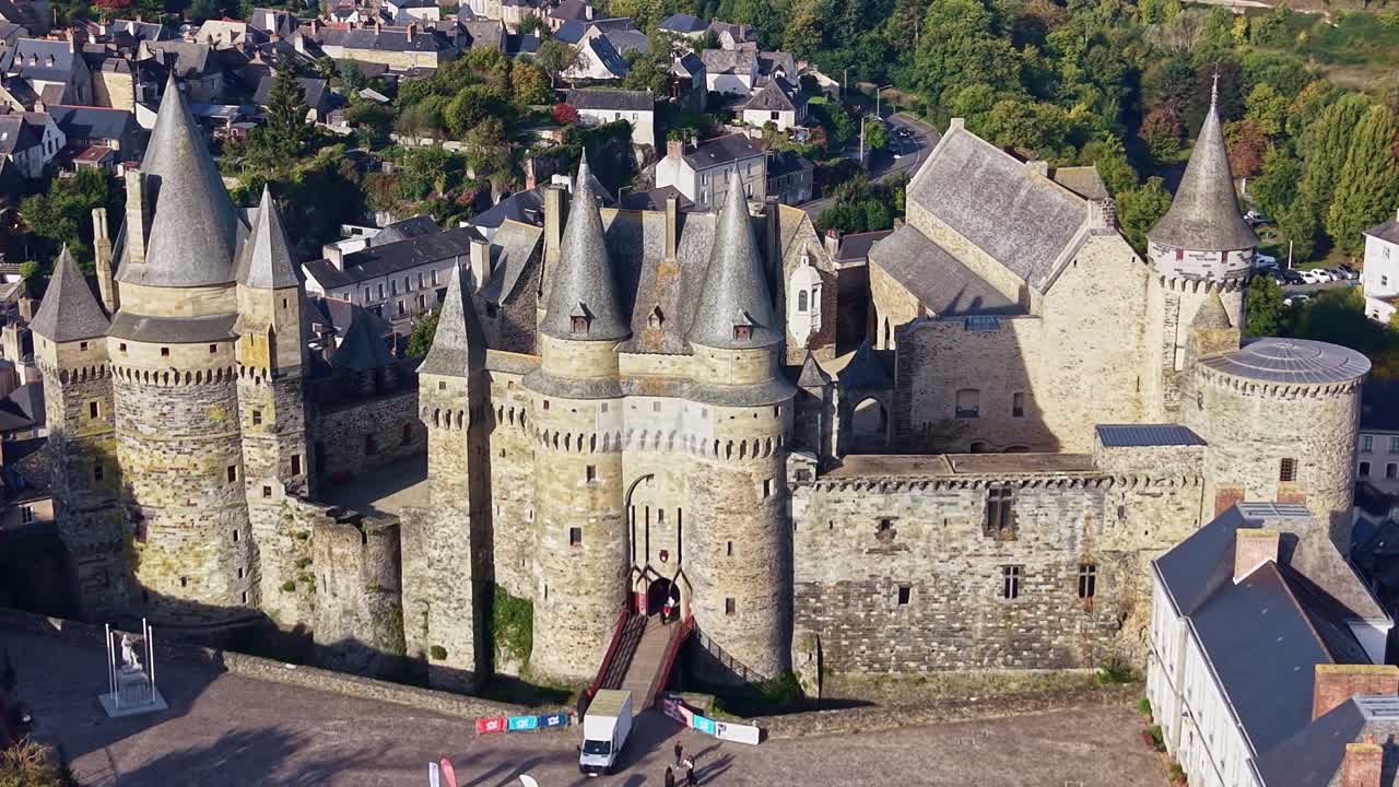 Drone shot showing the sunlit façade of castle of Vitré with the town and forest in the background