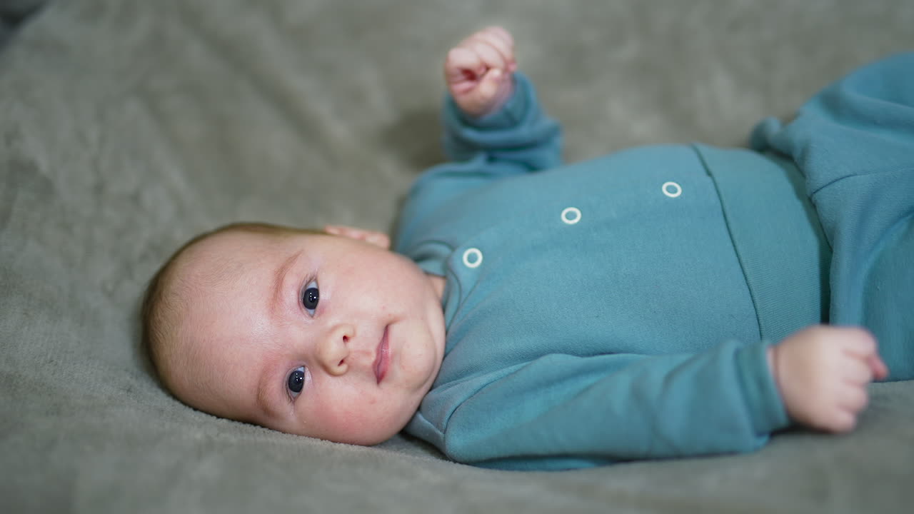 Little Caucasian toddler resting on the soft plaid. Sweet kid looking attentively into camera and tossing his hands. Close up.