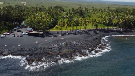 4k cinematic drone shot revealing waves crashing on punulu'u black sand beach on a sunny day on the big island of hawaii