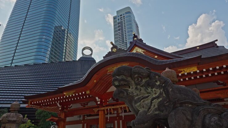 Um tradicional Santuário Nishikubo Hachimangu vermelho com um guardião de pedra, contrastando fortemente com modernos arranha-céus de vidro na paisagem urbana de Tóquio.